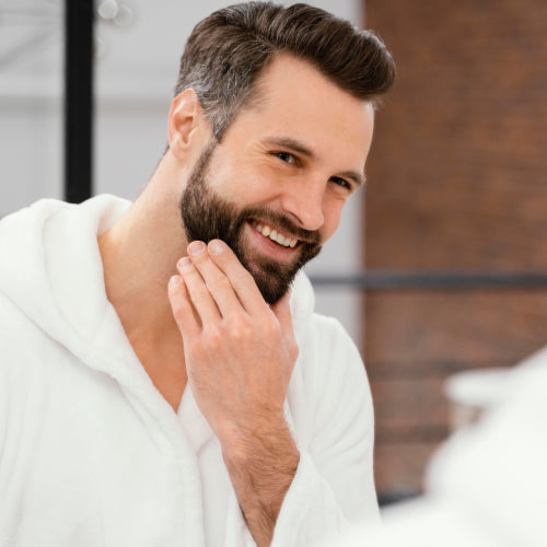 Homem sorri em frente ao espelho, ponderando se pode pintar a barba.
