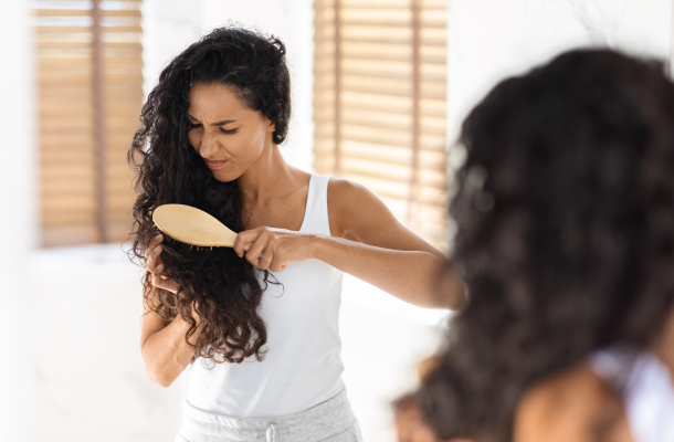 Jovem mulher morena irritada com cabelos emaranhados, usando escova de bambu