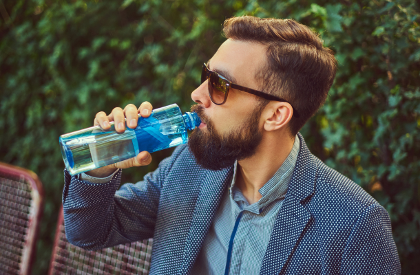 Homem com barba, óculos de sol e blazer a beber de uma garrafa da água
