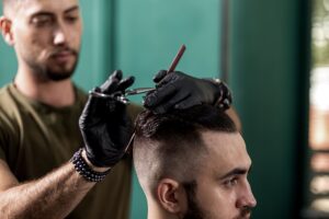 Barbeiro com luvas pretas, corta ao estilo fade cut, o cabelo de um homem em uma barbearia