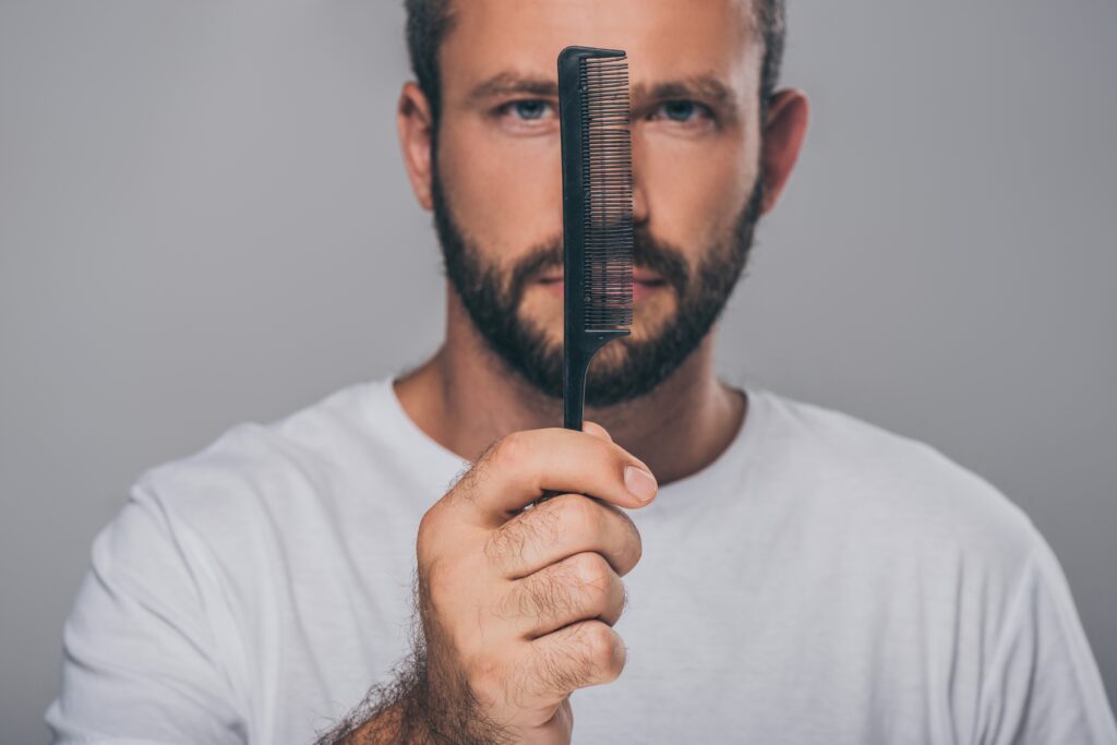 homem com barba segurando um pente e olhando para a câmara isolada